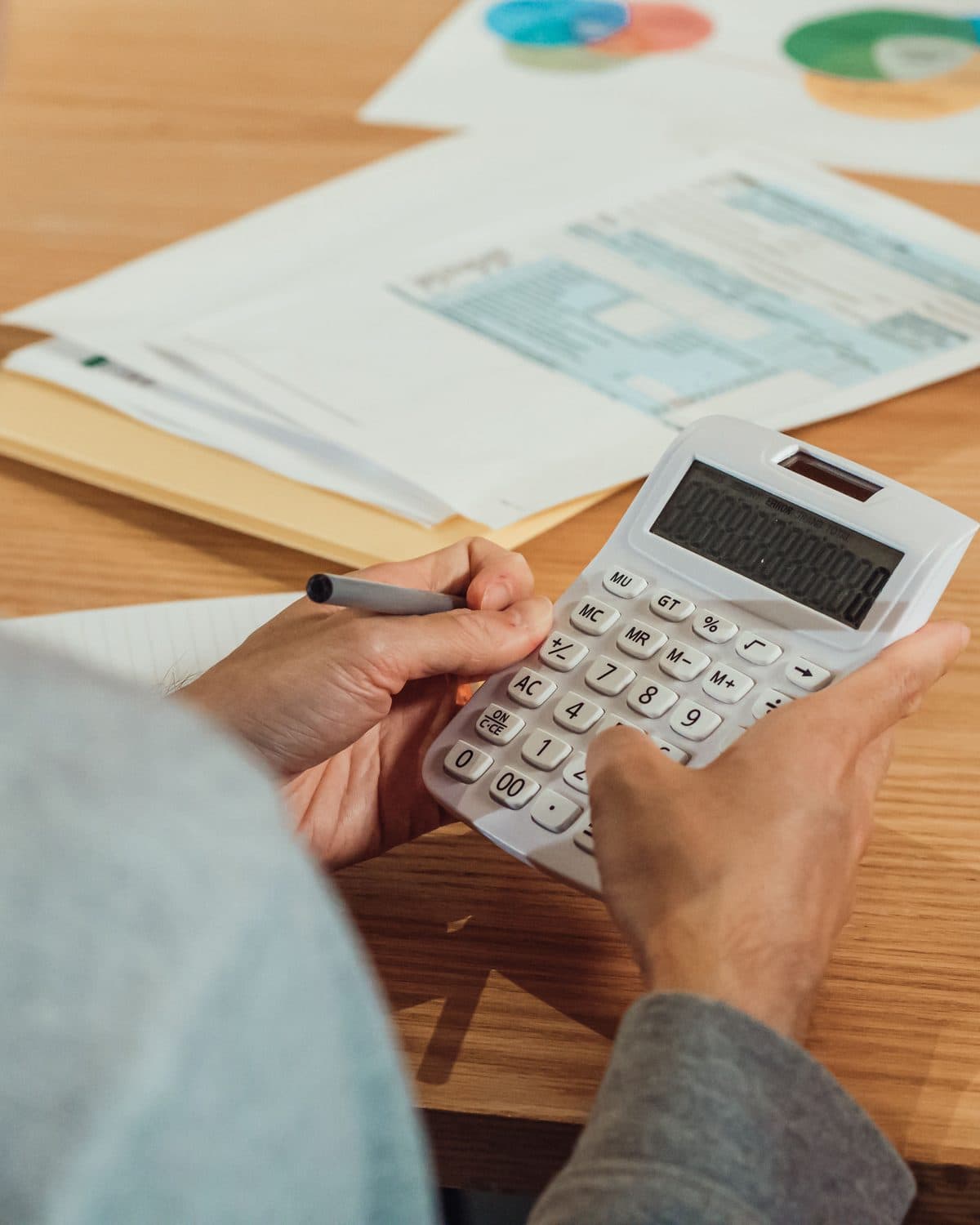Manos con una calculadora y una lapicera sobre un escritorio con facturas y planillas