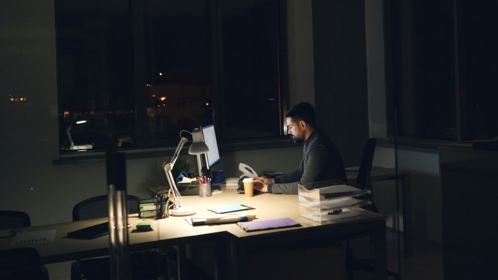 Hombre trabajando solo de noche en una oficina a oscuras, iluminado por la lámpara del escritorio